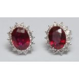 A pair of ruby and diamond cluster stud earings, mounted on 18k white gold, the oval central ruby