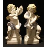 A pair of decorative ceramic cherubs, playing musical instruments, scantily clad, seated on fluted
