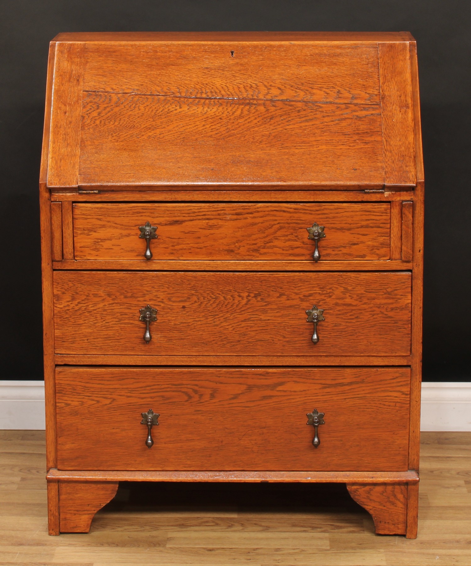 An early 20th century oak bureau, fall front enclosing a small drawer, pigeonholes and a small door,