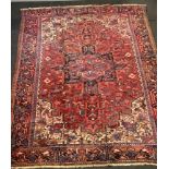 A hand woven Heriz carpet geometric designs in blue, cream and caramel on a red ground. 383cm x