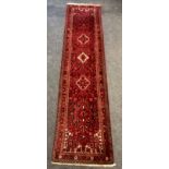 A hand woven Heriz runner decorated with geometric patterns in blue, cream and grey on a red ground.