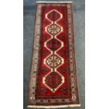 A hand woven Persian Sarab runner, geometric designs in hues of sage, blue and salmon on a red