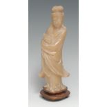 A Chinese soapstone carving, of Guanyin, she stands, holding a scroll, hardwood stand, 22cm high