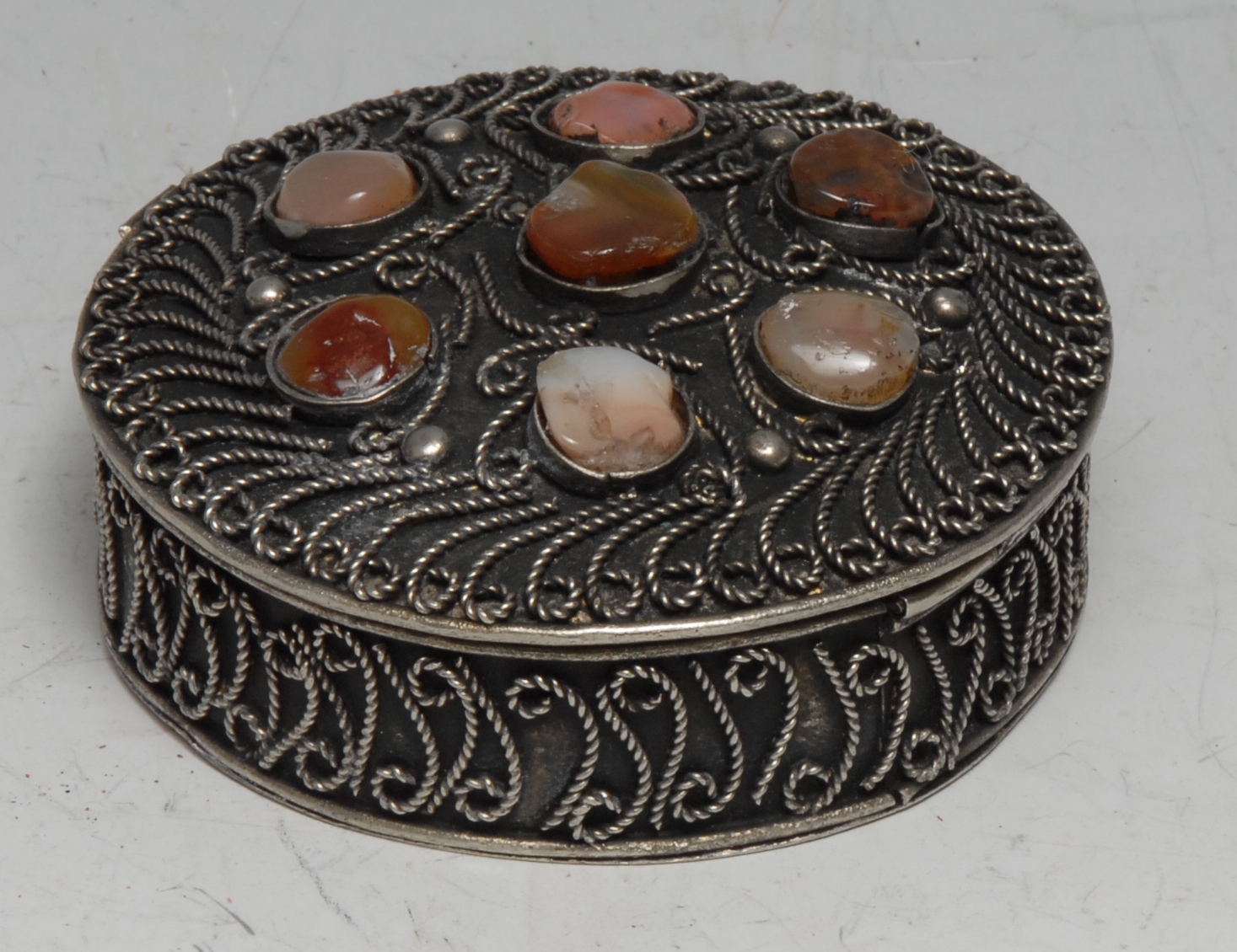 A Middle Eastern silver coloured metal circular box, applied with wirework scrolls and applied