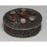 A Middle Eastern silver coloured metal circular box, applied with wirework scrolls and applied