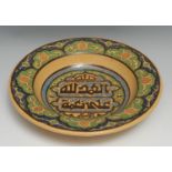 A Middle Eastern Islamic earthenware dish, inscribed with Arabic verseand painted with stylised