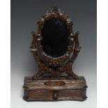 A Black Forest dressing glass, adjustable oval mirror plate, drawer to base, carved overall with