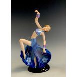 A 1930s German porcelain Art Deco figure of a dancing girl, flowing blue floral dress, arm aloft,
