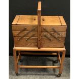 A oak concertina action sewing box trolley, with contents, 74.5cm high, 52cm long, 29.5cm wide.