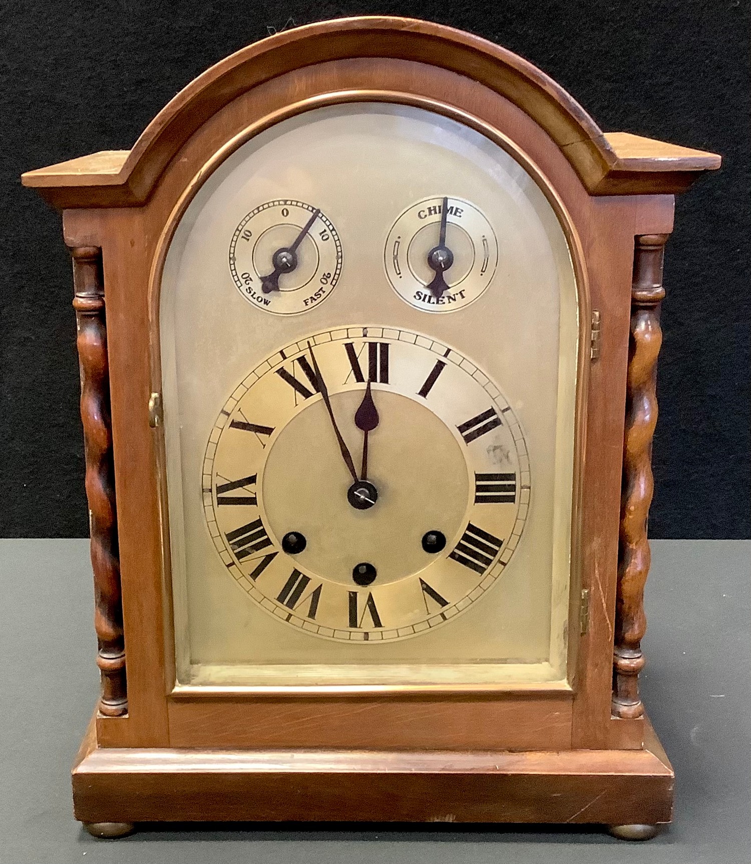 A mahogany dome top mantel clock, arched face, Roman numerals, flanked by barley twist columns,