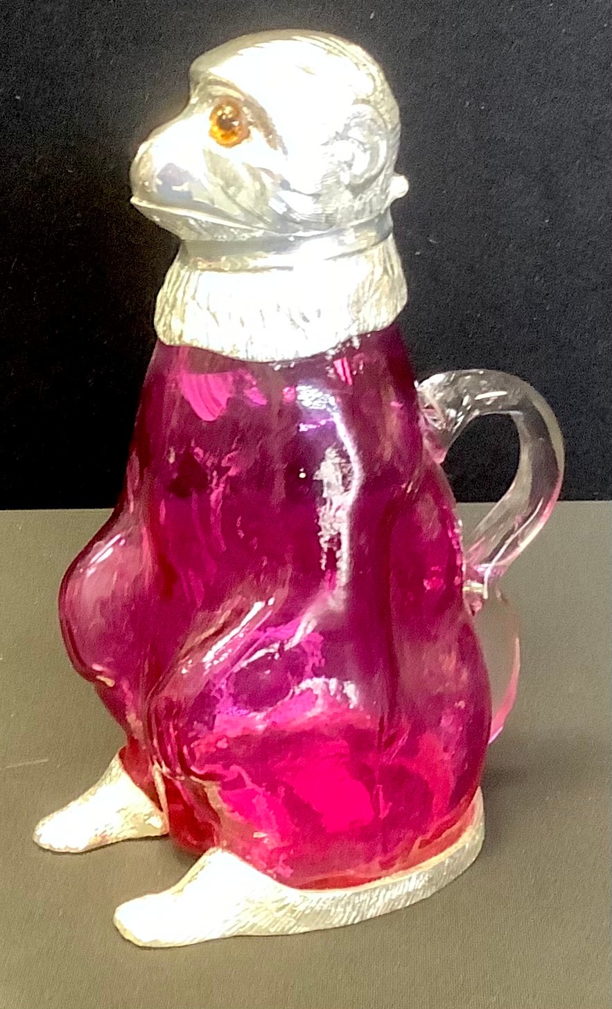 A contemporary silver plated mounted 'cranberry' coloured glass novelty claret jug, as a monkey,