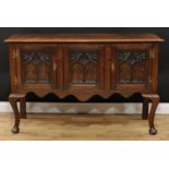 An oak low dresser or serving table, moulded rectangular top above three panel doors carved and