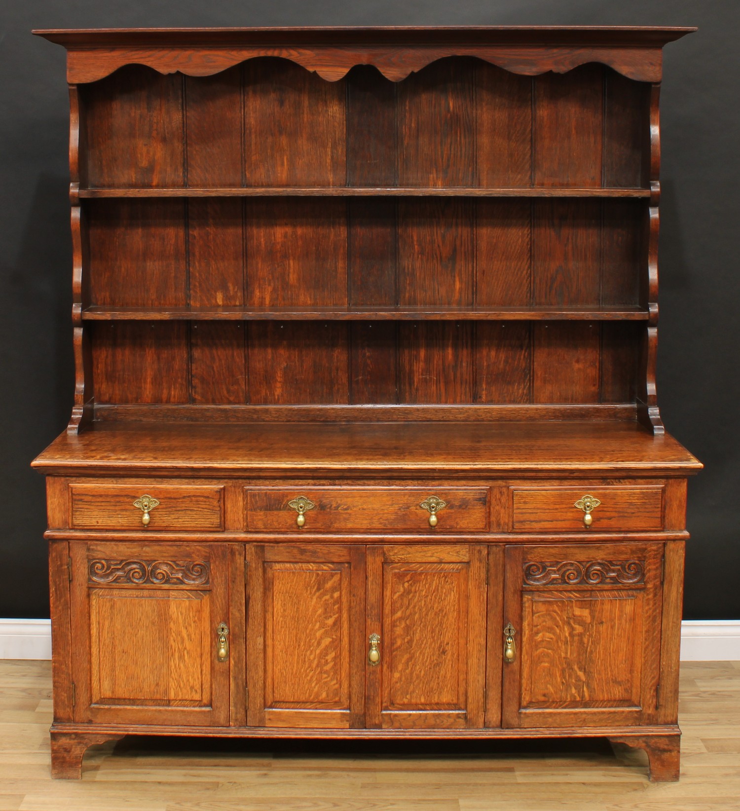 An oak dresser, outswept cornice above a pair of plate racks, the projecting base with three