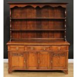 An oak dresser, outswept cornice above a pair of plate racks, the projecting base with three