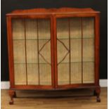 An early 20th century oak serpentine fronted display cabinet, shaped cresting, above a pair of