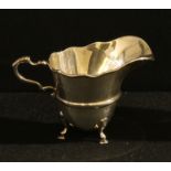 A George V silver helmet shaped cream jug, scroll handle, resting on three cabriole pad feet, 8cm,