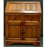 A mid 20th century oak bureau, linen fold fall front, above frieze drawer and pair of cupboard