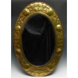 An Arts and Crafts brass oval looking glass, bevelled mirror plate, the border repousse chased