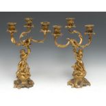 A pair of Rococo ormolu figural three-branch candelabra, cast with a pair of amorini, each seated on