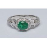 An emerald and diamond cluster ring, oval vibrant deep green emerald quarter claw set above a collar