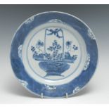 A Chinese circular dish, painted in tones of underglaze blue with a ribbon-tied basket of flowers,
