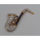 A diamond and sapphire saxophone brooch, pave encrusted with nine blue sapphires and over one