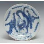 A Chinese circular dish, painted in tones of underglaze blue with a dragon amongst scrolling clouds,