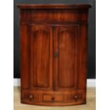 A George III mahogany bow front wall hanging corner cupboard, oversailing top above a pair of