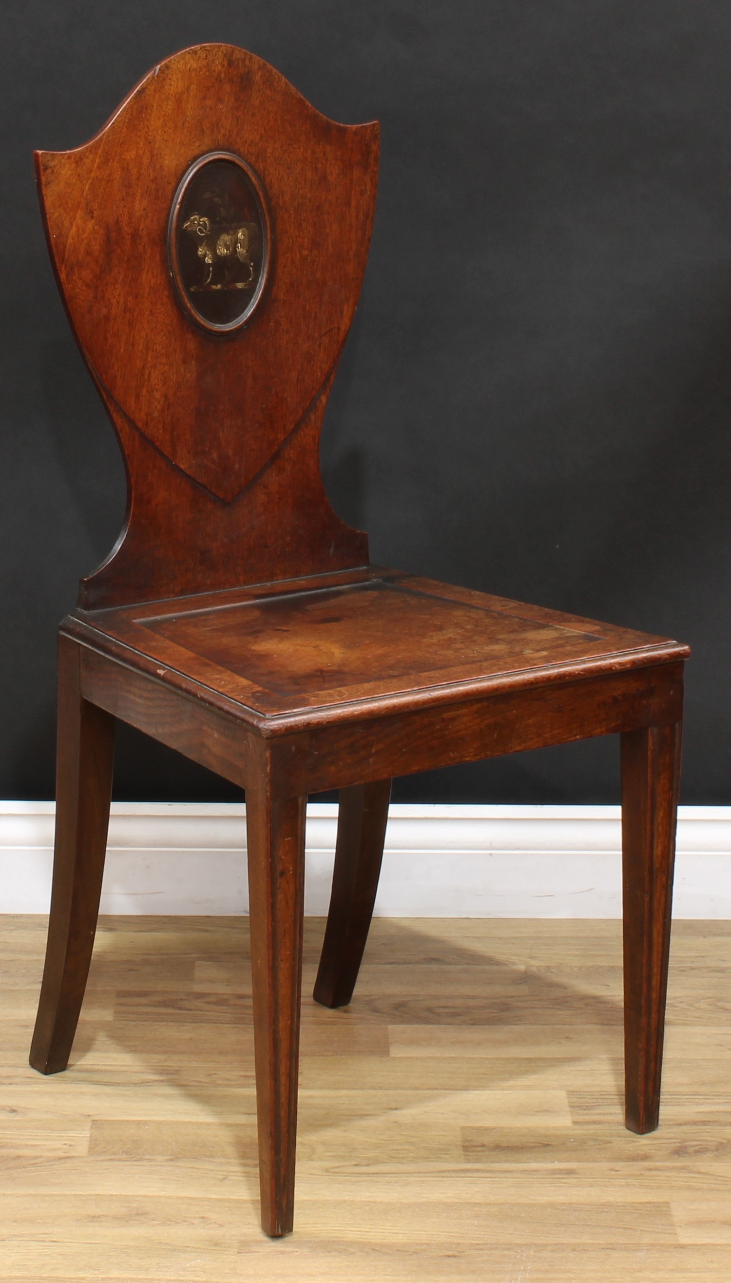 A George III mahogany Heraldic hall chair, shield shaped back with painted oval reserve, panel seat,