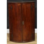 A George III mahogany banded oak wall hanging bow front corner cupboard, moulded cornice above a