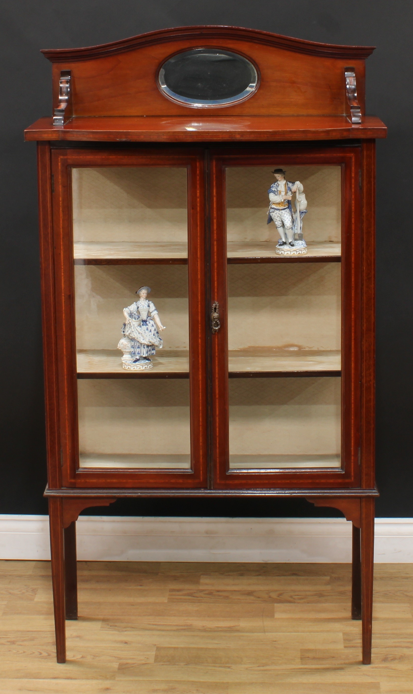 An Edwardian mahogany display cabinet, serpentine arched cresting with bevelled oval mirror, bow