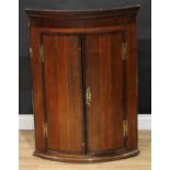 A George III mahogany crossbanded oak wall hanging bow front corner cupboard, moulded cornice