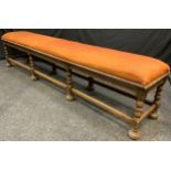 An early 20th oak long stool, stuffed-over seats, turned legs, bun feet, 54cm high, 237cm long, 43cm