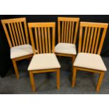 A set of four modern light wood dining chairs, cream upholstered seats.