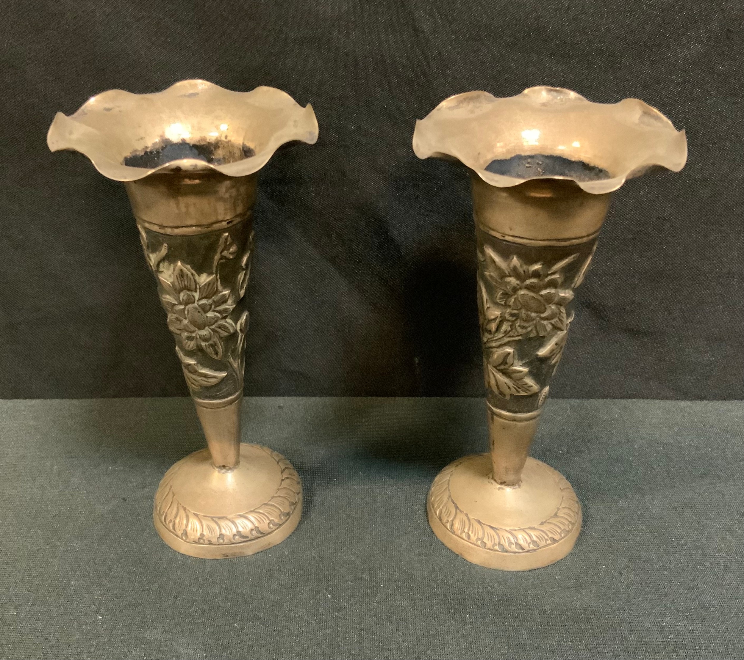 A pair of Indian silver coloured metal trumpet shaped vases, hand embossed with flowering foliage,