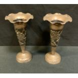 A pair of Indian silver coloured metal trumpet shaped vases, hand embossed with flowering foliage,
