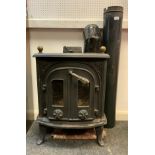 A cast iron log burner, ornate shaped rectangular body, brass finial top, two hinged front doors,