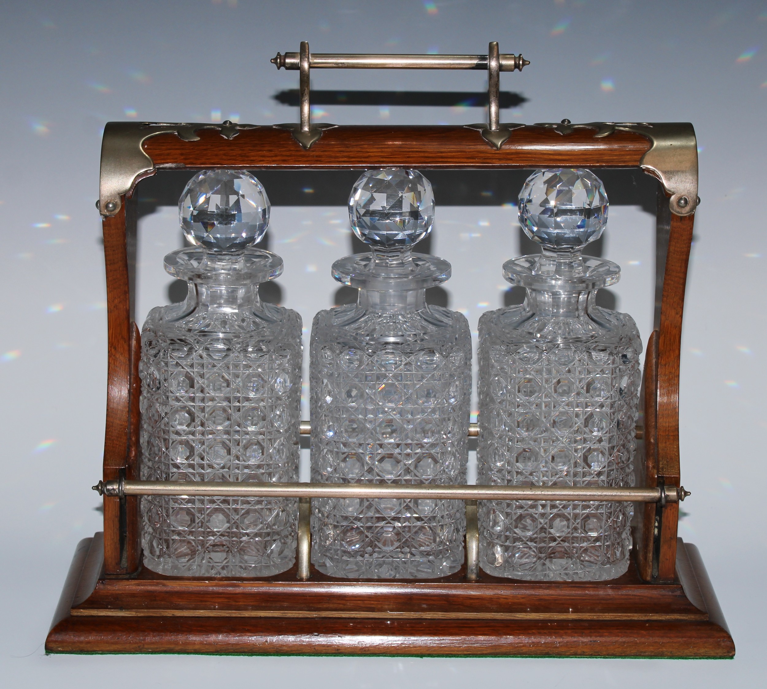 A late Victorian EPNS-mounted oak three-bottle tantalus, the unusual mechanism restraining the