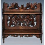 A Black Forest table-top two-shelf bookcase, the hinged sides restrained by hook-and-loops, carved