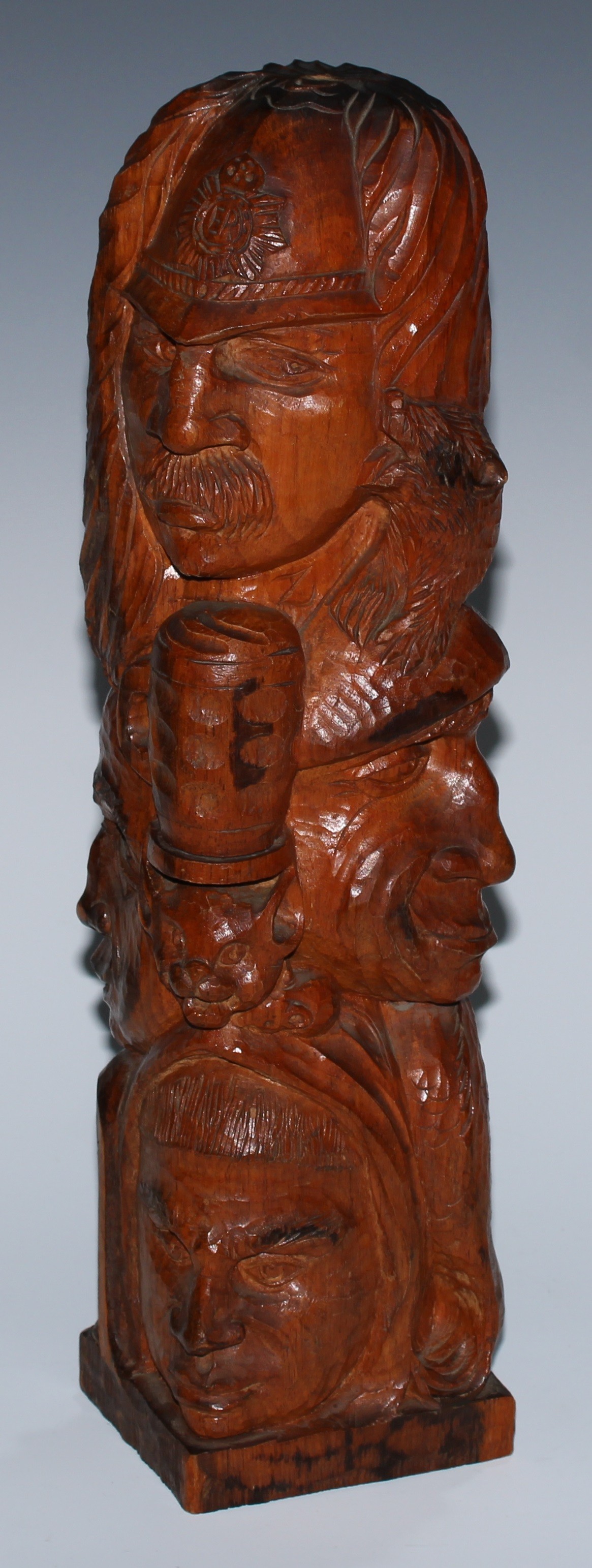 An adzed oak library desk sculpture, as a multi-bust totem pole, carved with heads from varying