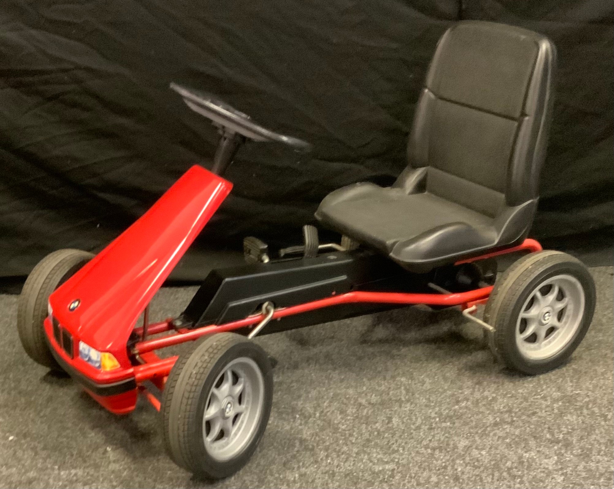 A BMW go-cart, peddle powered, plastic seat and tyres, red metal chassis, 92cm long, 56cm wide.