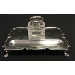 A George V silver desk stand, shaped rectangular top, moulded rim, pen tray front, cut glass inkwell