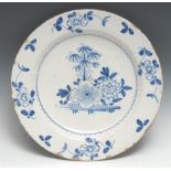 An English 18th century Delft charger, decorated in underlaze blue with stylised flowers and bamboo,