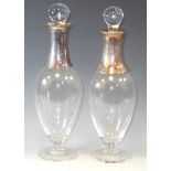 A composed pair of EPNS mounted clear glass slender ovoid decanters with globular stoppers, tall