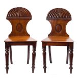 A pair of early 19th Century mahogany hall chairs: the backs with reeded lunette crestings and
