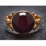 A cabochon garnet single-stone ring: in closed-back setting and between splayed shoulders,
