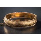 A 9ct gold hinged bangle: with attached safety chain, approximately 19gms gross weight,