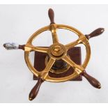 A small brass ship's helm: of five spokes with teak grips, mounted on a wooden plinth,