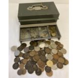 A green metal cash tin containing a collection of antique and vintage coins.