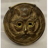 A circular shaped brass vesta case with cat face detail to each side.